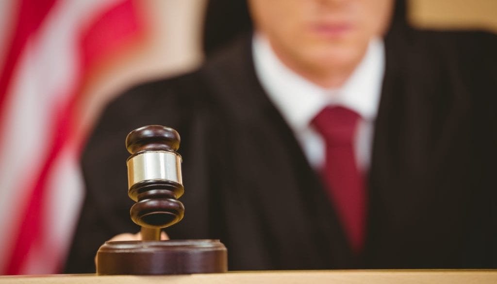 Serious judge about to bang gavel on sounding block in the court room